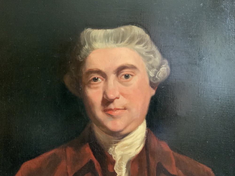 An antique oil painting depicting a half-length portrait of a gentleman in a dark red coat, set within a carved gilded frame with a metal title plaque at the bottom. View V