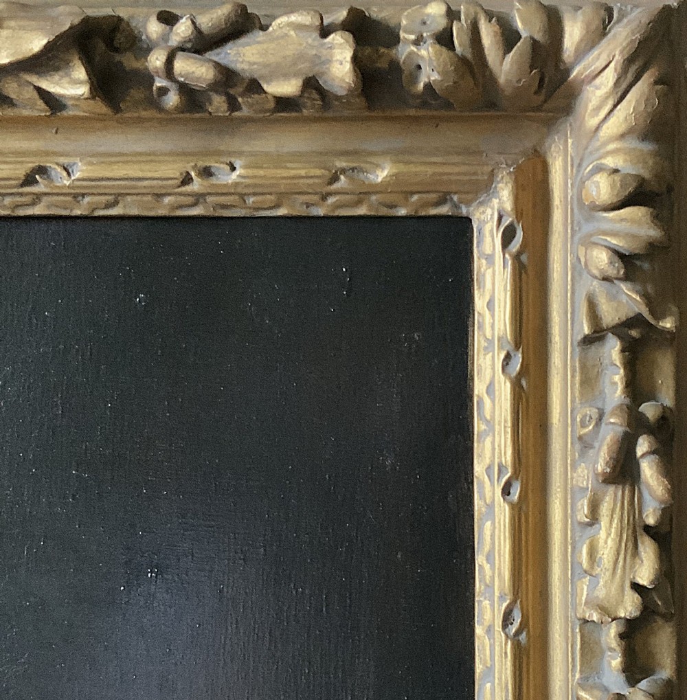 An antique oil painting depicting a half-length portrait of a gentleman in a dark red coat, set within a carved gilded frame with a metal title plaque at the bottom. View X