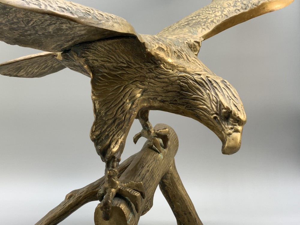A cast brass sculpture depicting an eagle with outstretched wings perched atop a detailed log branch. View IV