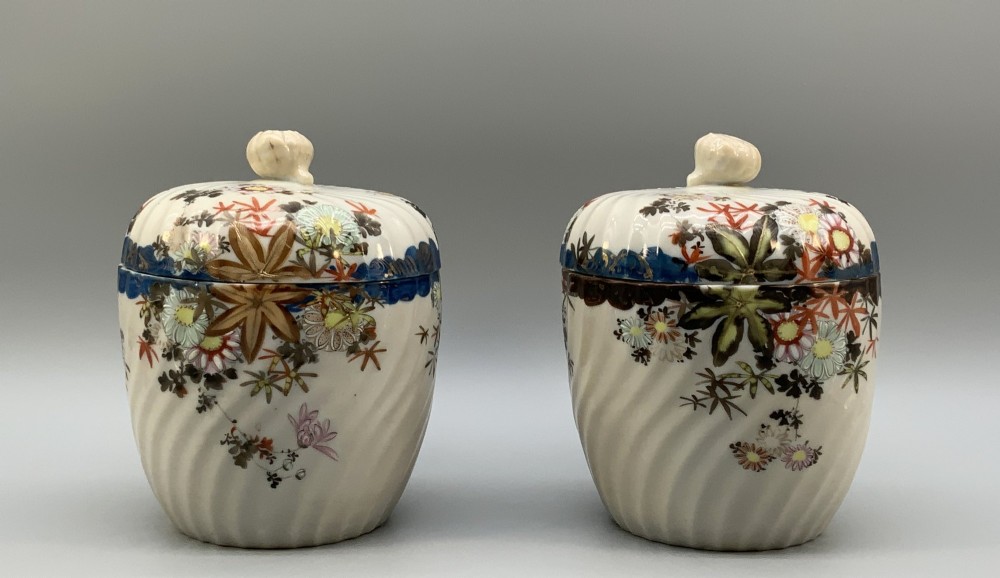 A pair of 19th-century Japanese cream porcelain lidded jars featuring spiralled fluted bodies and hand-painted polychrome floral decoration with sculpted finials.