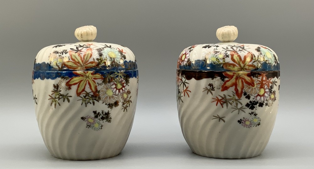 A pair of 19th-century Japanese cream porcelain lidded jars featuring spiralled fluted bodies and hand-painted polychrome floral decoration with sculpted finials. View V