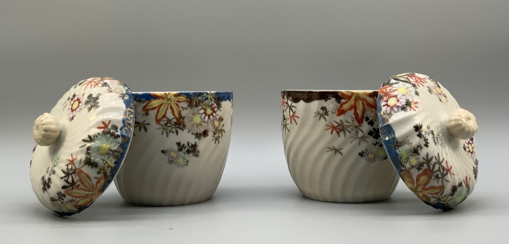 A pair of 19th-century Japanese cream porcelain lidded jars featuring spiralled fluted bodies and hand-painted polychrome floral decoration with sculpted finials. View VI