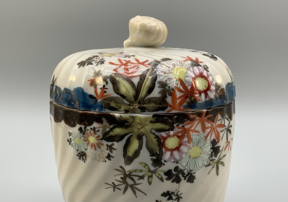 A pair of 19th-century Japanese cream porcelain lidded jars featuring spiralled fluted bodies and hand-painted polychrome floral decoration with sculpted finials. View X