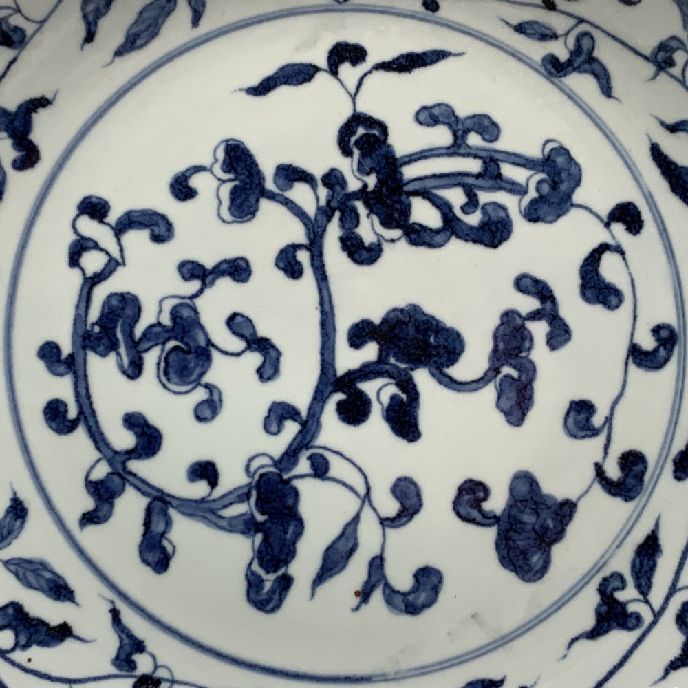 A circular Chinese blue and white porcelain charger decorated with hand-painted scrolling foliage and floral motifs, resting on a dark wooden stand. View V