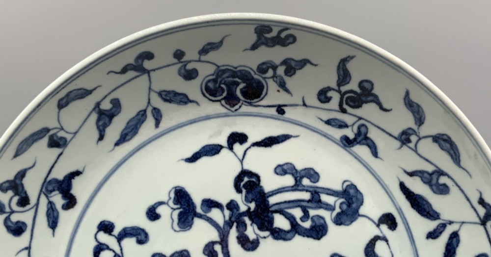 A circular Chinese blue and white porcelain charger decorated with hand-painted scrolling foliage and floral motifs, resting on a dark wooden stand. View VI