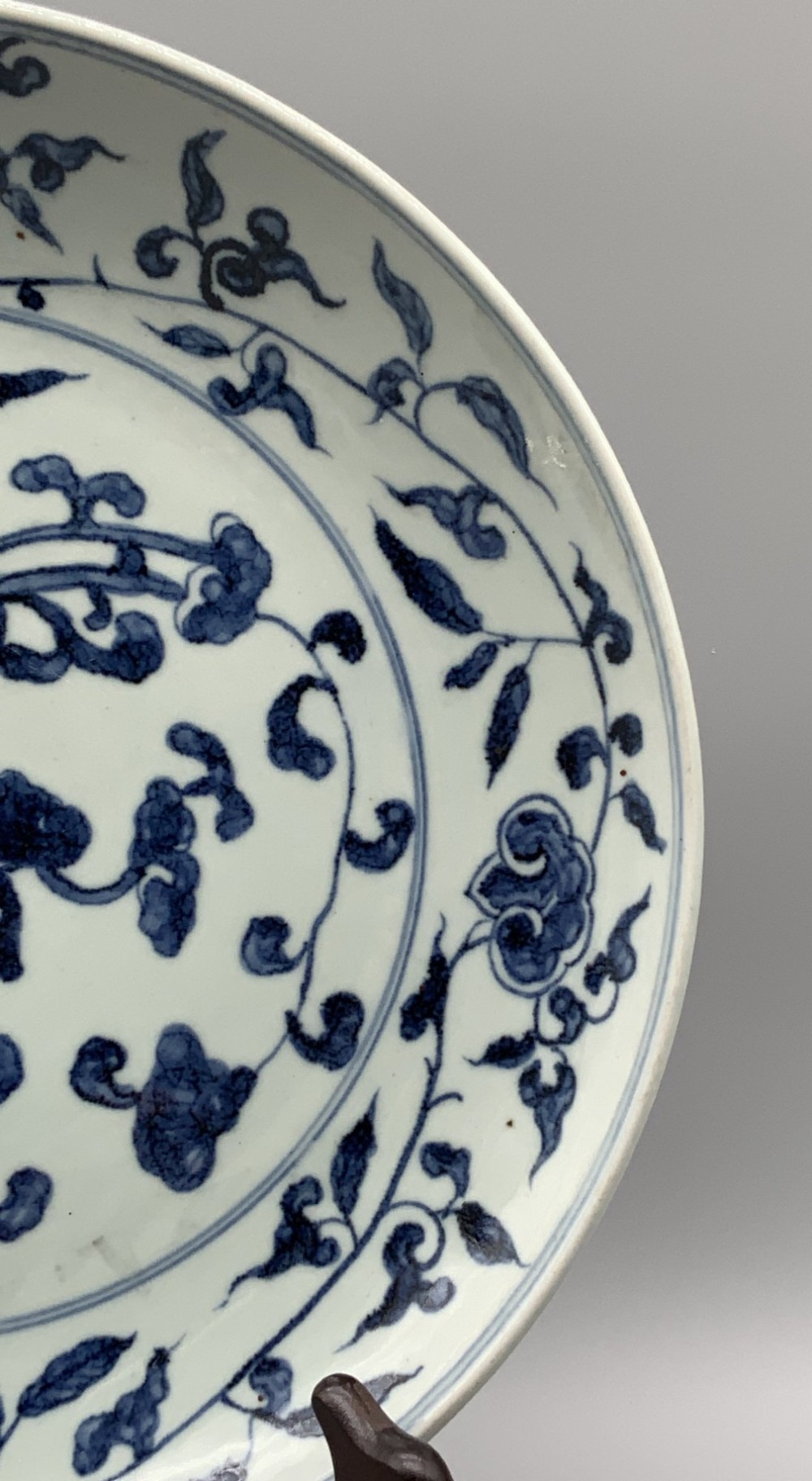 A circular Chinese blue and white porcelain charger decorated with hand-painted scrolling foliage and floral motifs, resting on a dark wooden stand. View VIII
