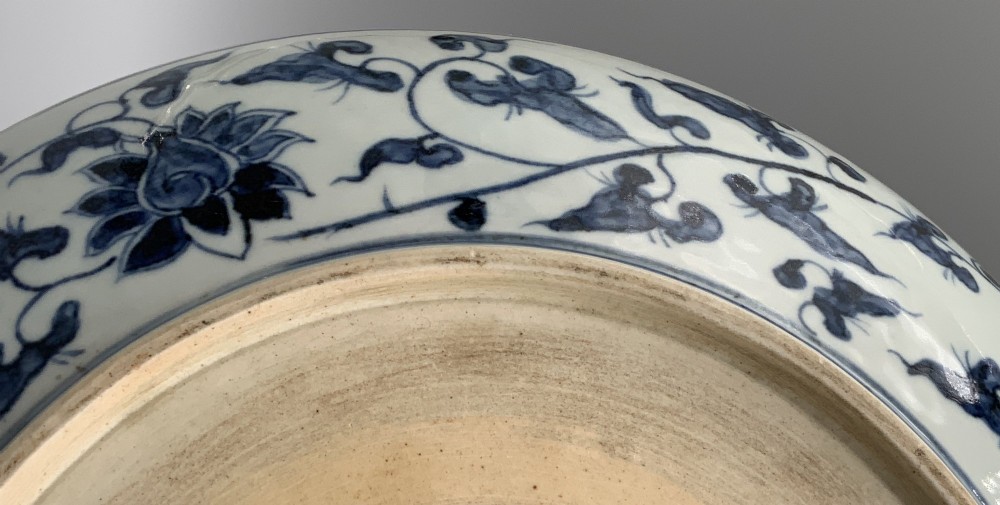 A circular Chinese blue and white porcelain charger decorated with hand-painted scrolling foliage and floral motifs, resting on a dark wooden stand. View XIV