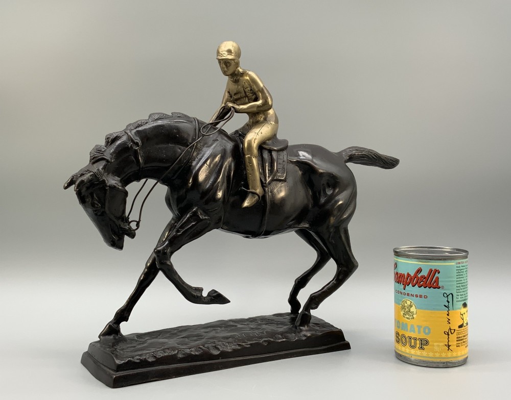 A patinated bronze sculpture depicting a racehorse and jockey mid-stride set upon a textured rectangular bronze base. View III