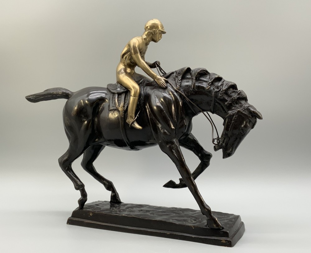 A patinated bronze sculpture depicting a racehorse and jockey mid-stride set upon a textured rectangular bronze base. View VII