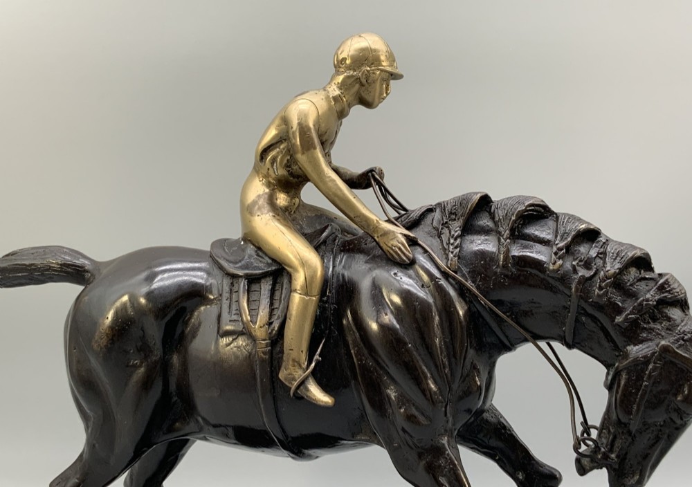 A patinated bronze sculpture depicting a racehorse and jockey mid-stride set upon a textured rectangular bronze base. View VIII