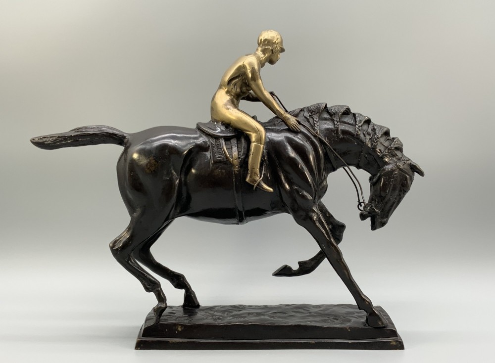 A patinated bronze sculpture depicting a racehorse and jockey mid-stride set upon a textured rectangular bronze base. View IX