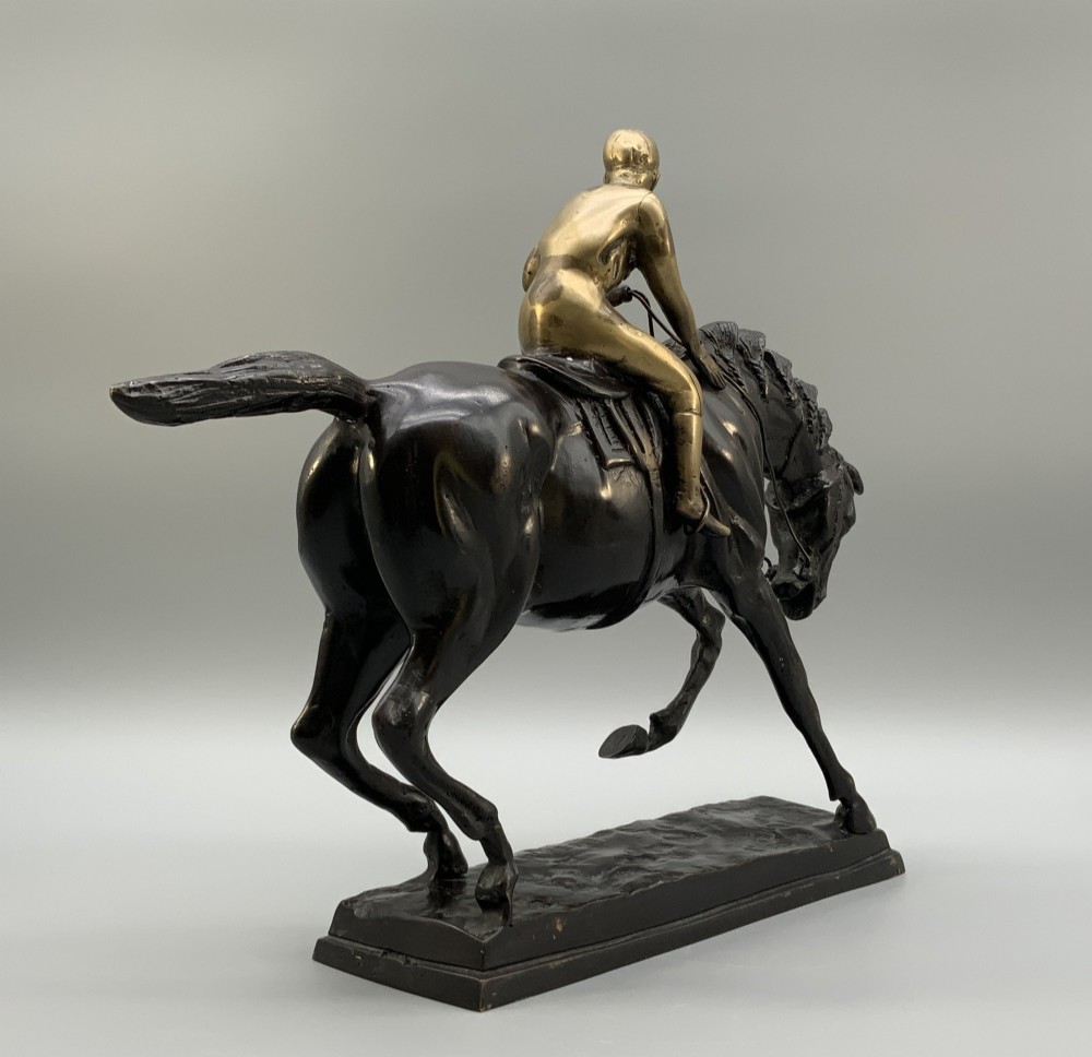 A patinated bronze sculpture depicting a racehorse and jockey mid-stride set upon a textured rectangular bronze base. View X