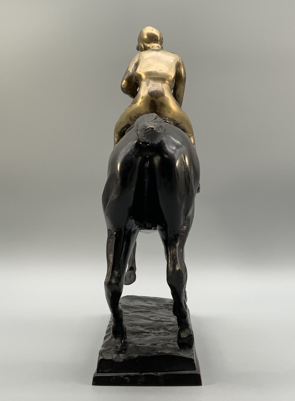 A patinated bronze sculpture depicting a racehorse and jockey mid-stride set upon a textured rectangular bronze base. View XI