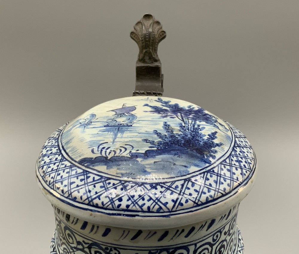 An eighteenth-century blue and white Dutch Delftware ceramic jug decorated with hand-painted figures, complete with a fitted pewter lid. View X