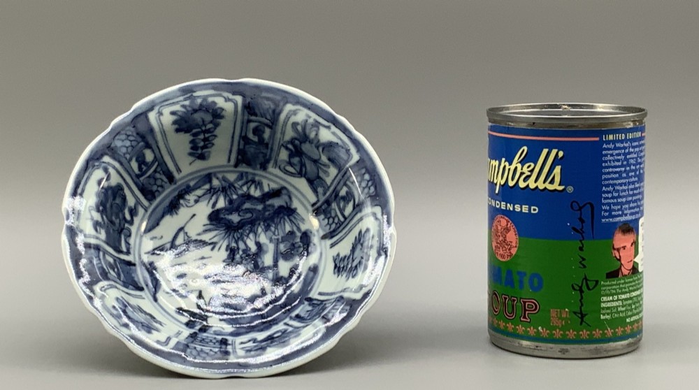 A circular porcelain bowl with a lobed edge, decorated in cobalt blue underglaze featuring a central landscape surrounded by panelled floral reserves. View III