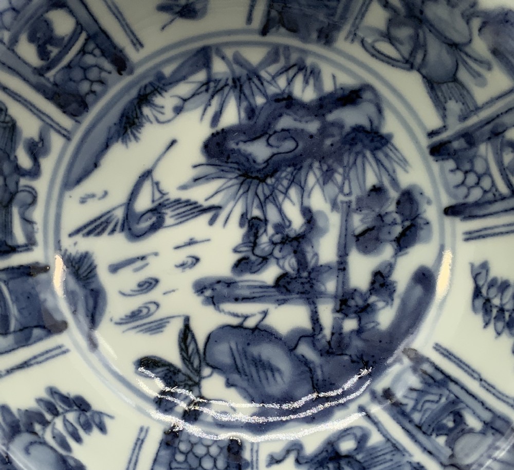 A circular porcelain bowl with a lobed edge, decorated in cobalt blue underglaze featuring a central landscape surrounded by panelled floral reserves. View IV