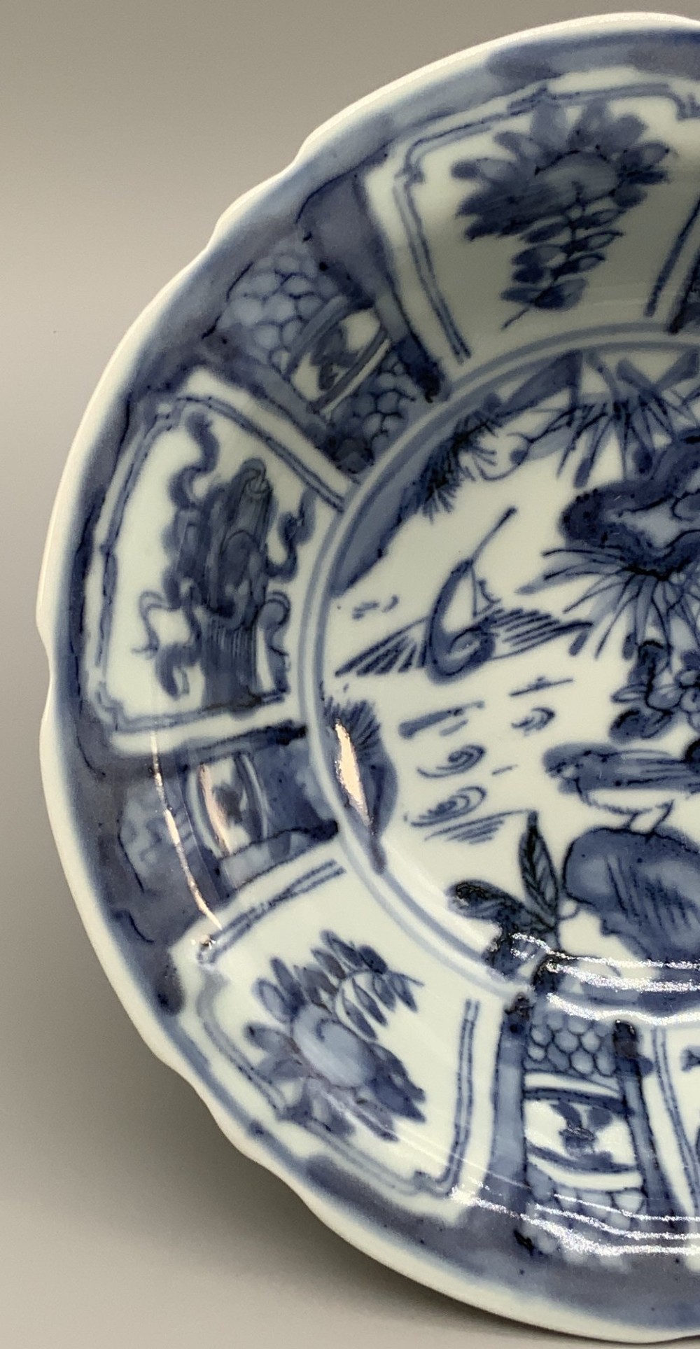 A circular porcelain bowl with a lobed edge, decorated in cobalt blue underglaze featuring a central landscape surrounded by panelled floral reserves. View VIII