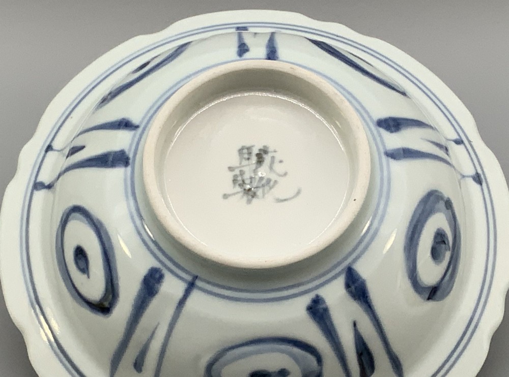 A circular porcelain bowl with a lobed edge, decorated in cobalt blue underglaze featuring a central landscape surrounded by panelled floral reserves. View XI