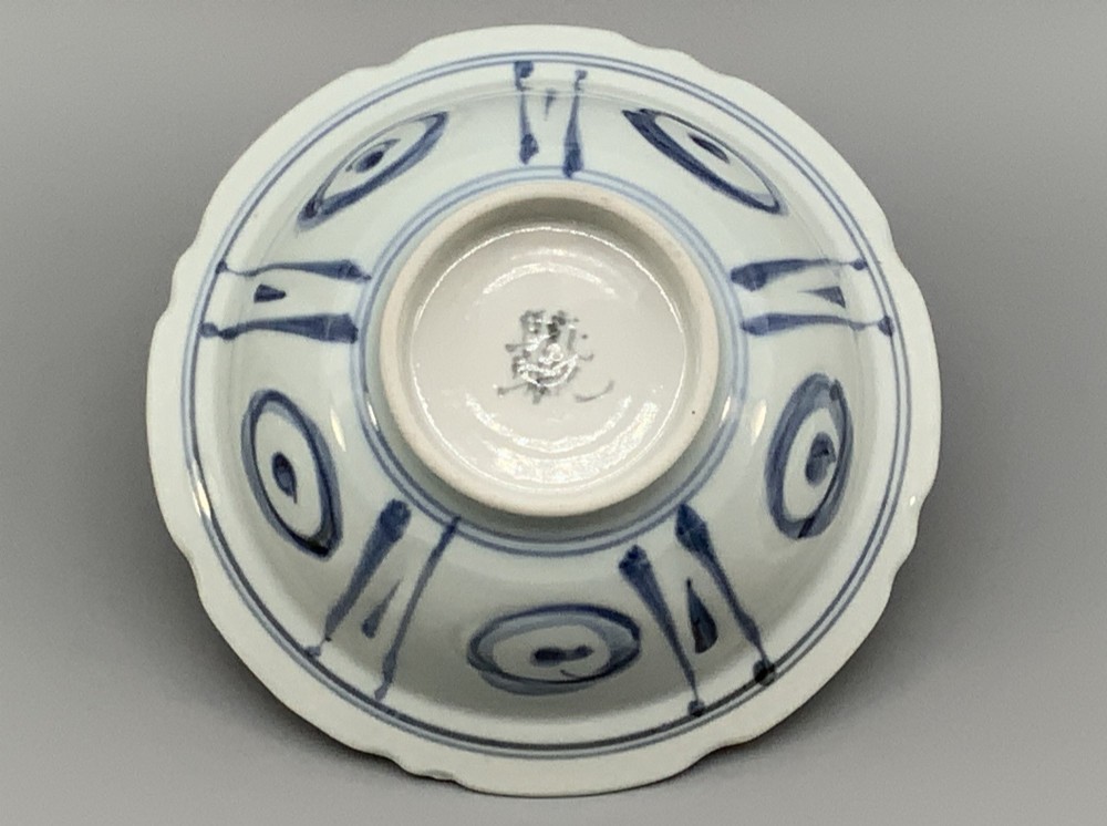 A circular porcelain bowl with a lobed edge, decorated in cobalt blue underglaze featuring a central landscape surrounded by panelled floral reserves. View XII
