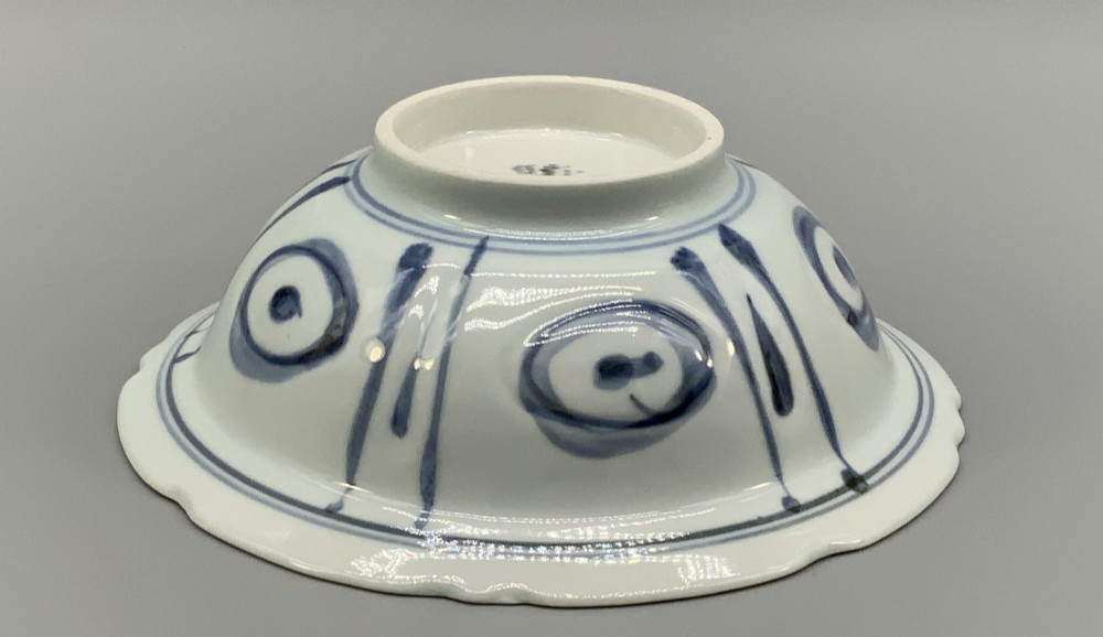 A circular porcelain bowl with a lobed edge, decorated in cobalt blue underglaze featuring a central landscape surrounded by panelled floral reserves. View XIII
