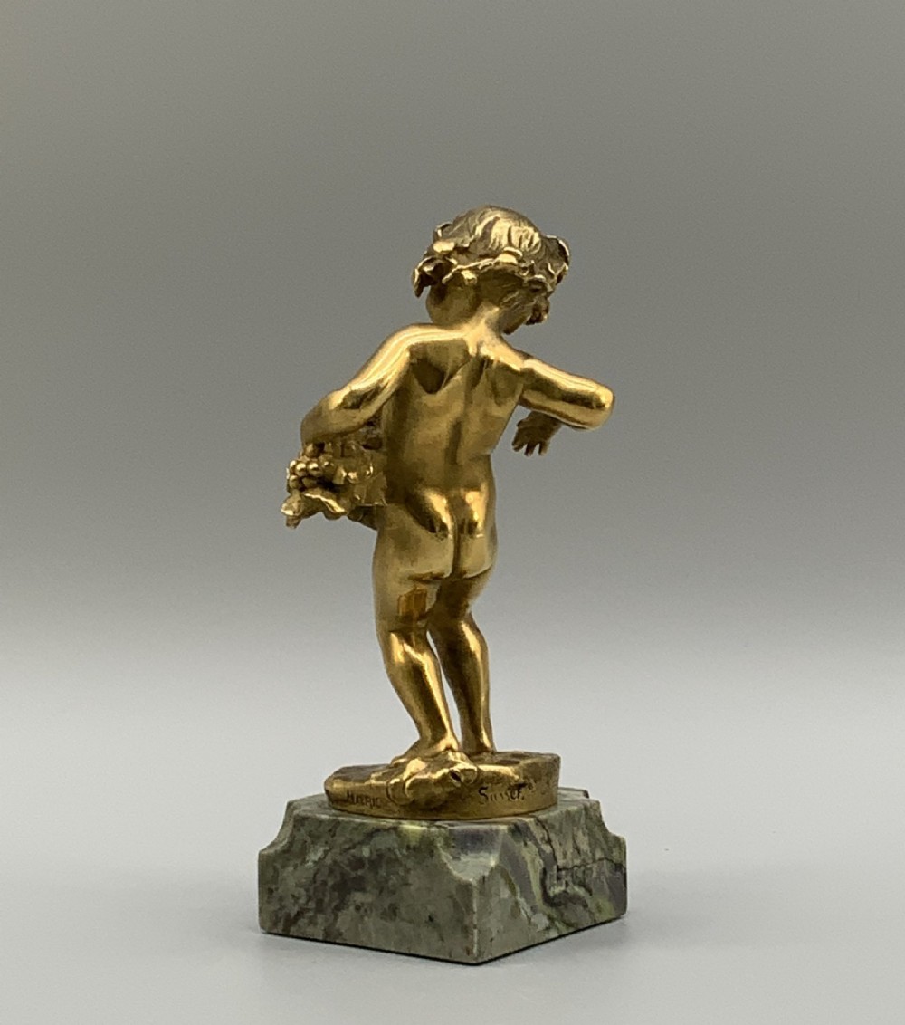 A small gilt bronze sculpture depicting an infant Bacchus holding a bunch of grapes, set upon a square green marble plinth. View VI