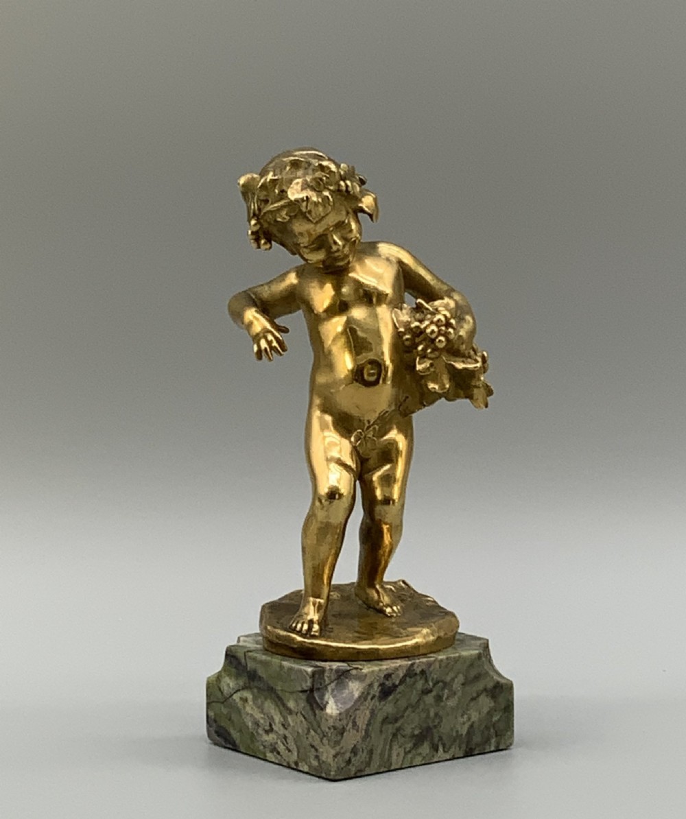 A small gilt bronze sculpture depicting an infant Bacchus holding a bunch of grapes, set upon a square green marble plinth. View IX