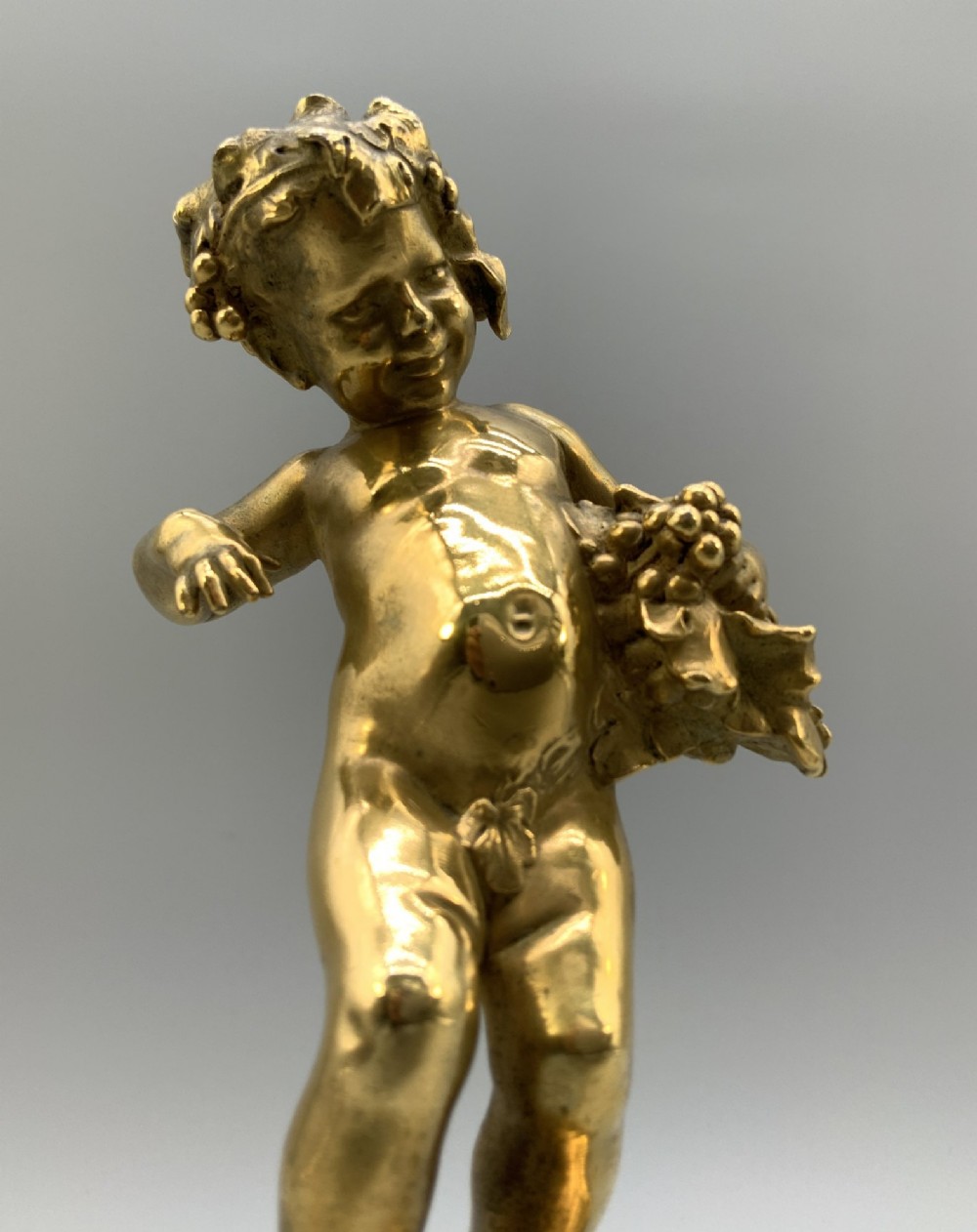 A small gilt bronze sculpture depicting an infant Bacchus holding a bunch of grapes, set upon a square green marble plinth. View X