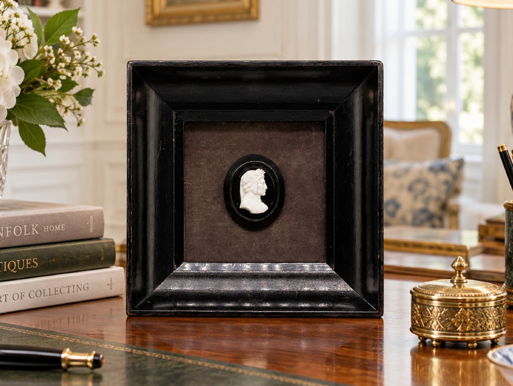 A small carved white classical profile portrait cameo mounted on a dark background within a deep black ebonised square frame. View II