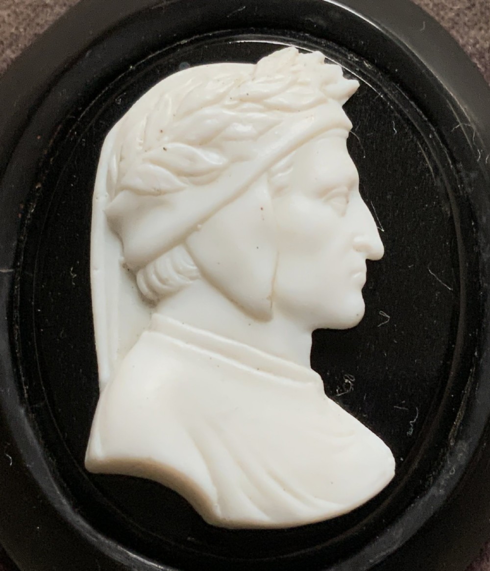 A small carved white classical profile portrait cameo mounted on a dark background within a deep black ebonised square frame. View III