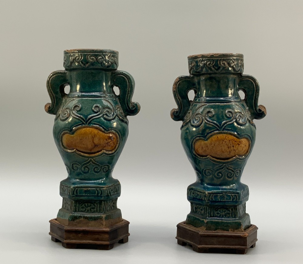 A pair of early seventeenth-century Chinese ceramic vases featuring turquoise glaze, amber reserves, relief scrollwork, and wooden bases.