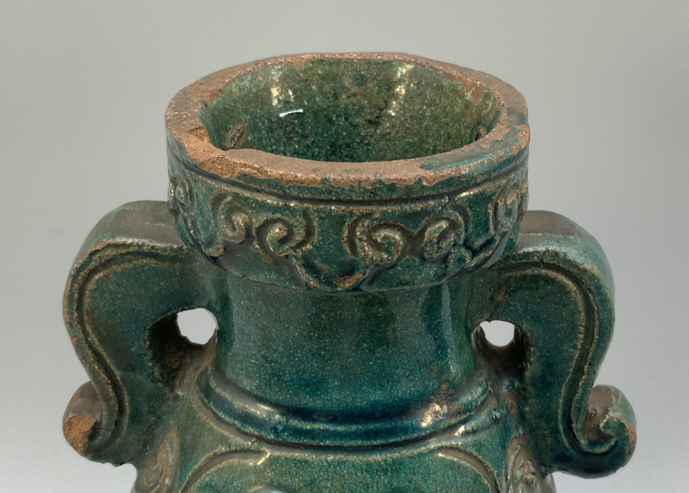 A pair of early seventeenth-century Chinese ceramic vases featuring turquoise glaze, amber reserves, relief scrollwork, and wooden bases. View X