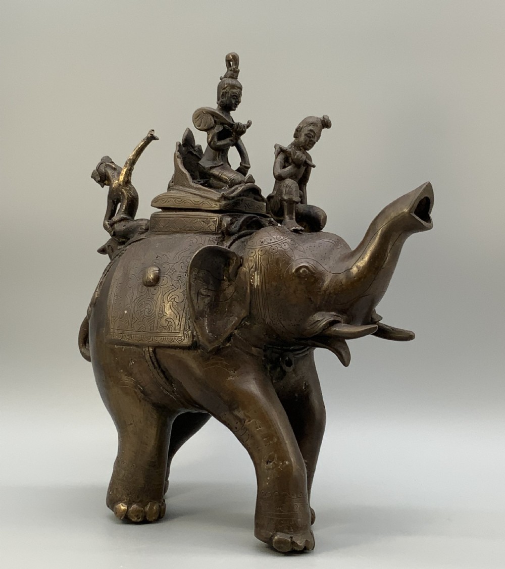 A dark bronze 19th-century sculpture depicting an elephant with engraved decorative trappings and riders seated on its back.