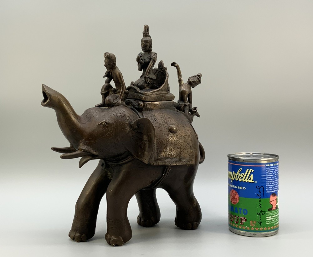 A dark bronze 19th-century sculpture depicting an elephant with engraved decorative trappings and riders seated on its back. View III