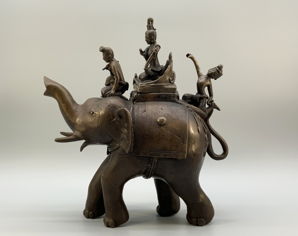 A dark bronze 19th-century sculpture depicting an elephant with engraved decorative trappings and riders seated on its back. View IV