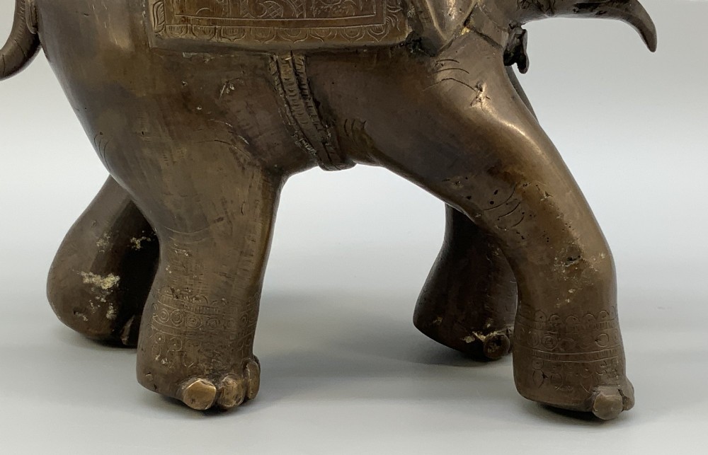 A dark bronze 19th-century sculpture depicting an elephant with engraved decorative trappings and riders seated on its back. View X
