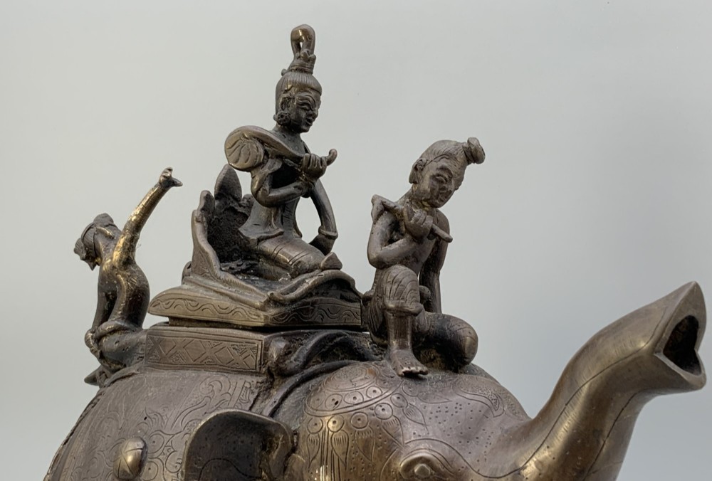 A dark bronze 19th-century sculpture depicting an elephant with engraved decorative trappings and riders seated on its back. View XI