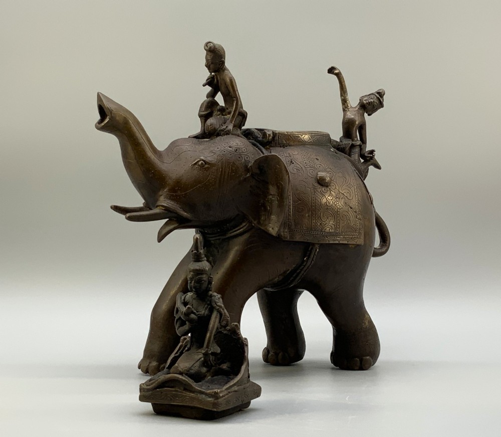 A dark bronze 19th-century sculpture depicting an elephant with engraved decorative trappings and riders seated on its back. View XIII