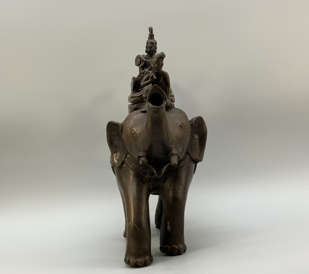 A dark bronze 19th-century sculpture depicting an elephant with engraved decorative trappings and riders seated on its back. View XIV