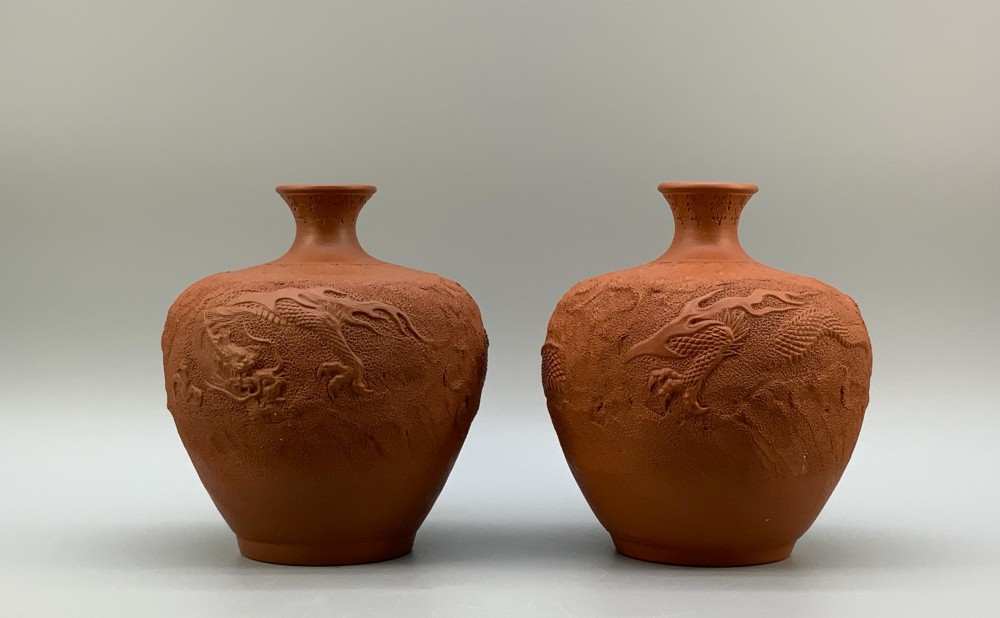 A pair of unglazed terracotta red clay vases featuring detailed relief carvings of dragons with narrow flared necks.