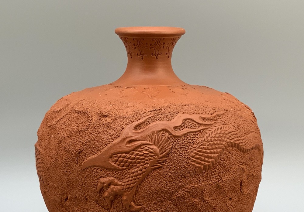 A pair of unglazed terracotta red clay vases featuring detailed relief carvings of dragons with narrow flared necks. View V