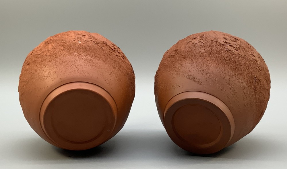A pair of unglazed terracotta red clay vases featuring detailed relief carvings of dragons with narrow flared necks. View X