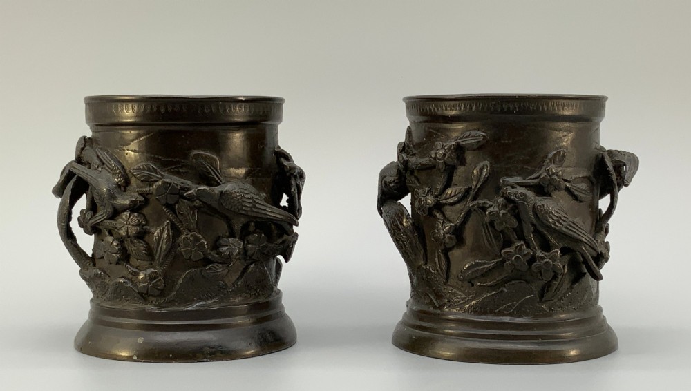A pair of cylindrical dark patinated bronze vases featuring raised relief depictions of birds perched amongst cherry blossom branches.