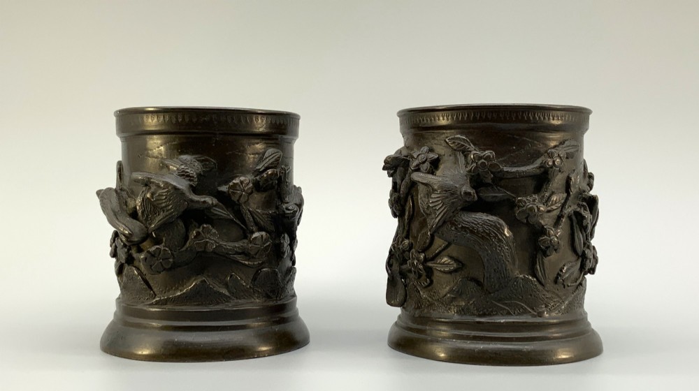 A pair of cylindrical dark patinated bronze vases featuring raised relief depictions of birds perched amongst cherry blossom branches. View VI