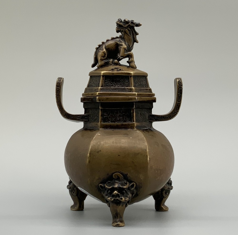 A late Qing dynasty hexagonal bronze tripod censer featuring upright side handles, a removable cover topped with a mythical beast finial, and feet shaped as animal masks. View III