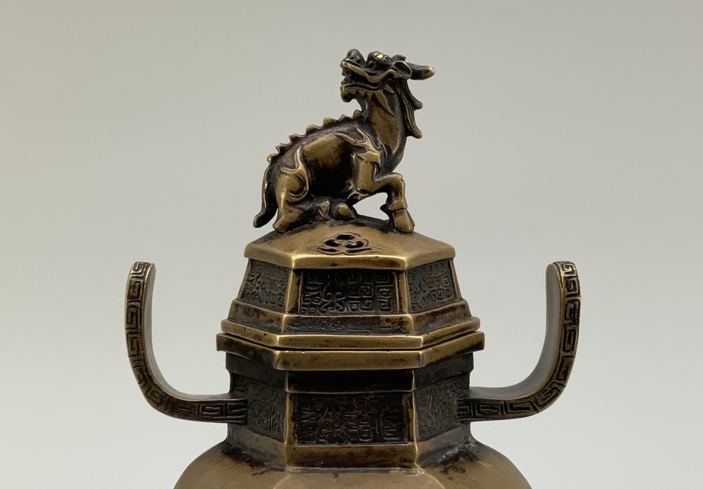 A late Qing dynasty hexagonal bronze tripod censer featuring upright side handles, a removable cover topped with a mythical beast finial, and feet shaped as animal masks. View IV