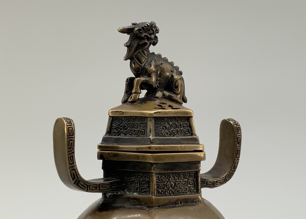 A late Qing dynasty hexagonal bronze tripod censer featuring upright side handles, a removable cover topped with a mythical beast finial, and feet shaped as animal masks. View IX