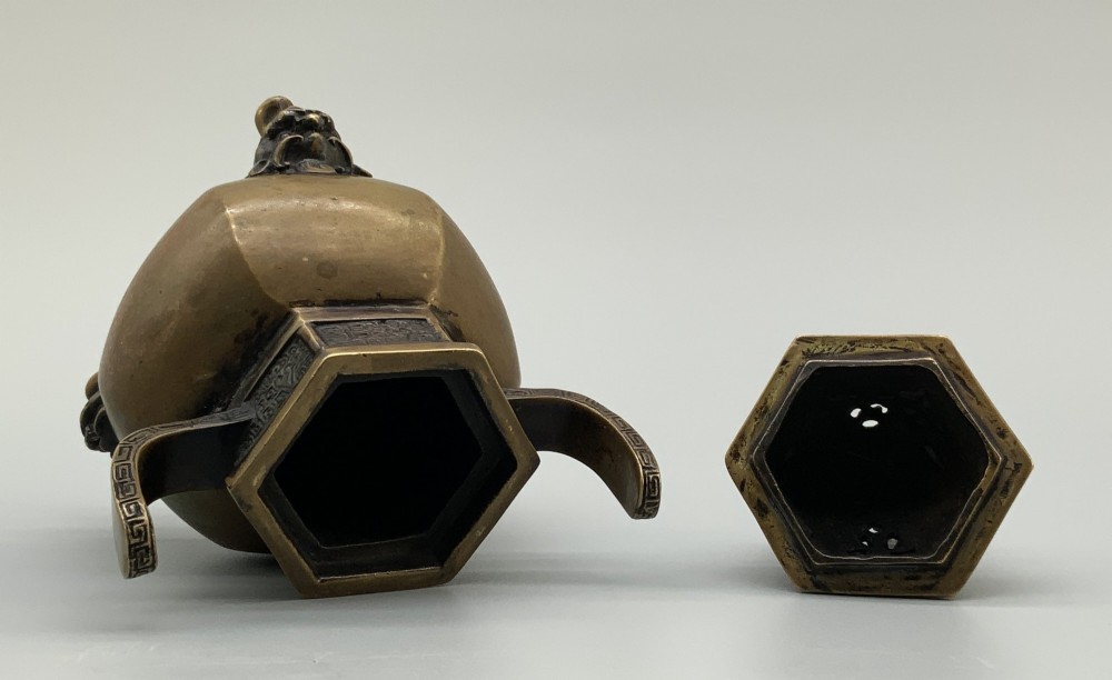 A late Qing dynasty hexagonal bronze tripod censer featuring upright side handles, a removable cover topped with a mythical beast finial, and feet shaped as animal masks. View X