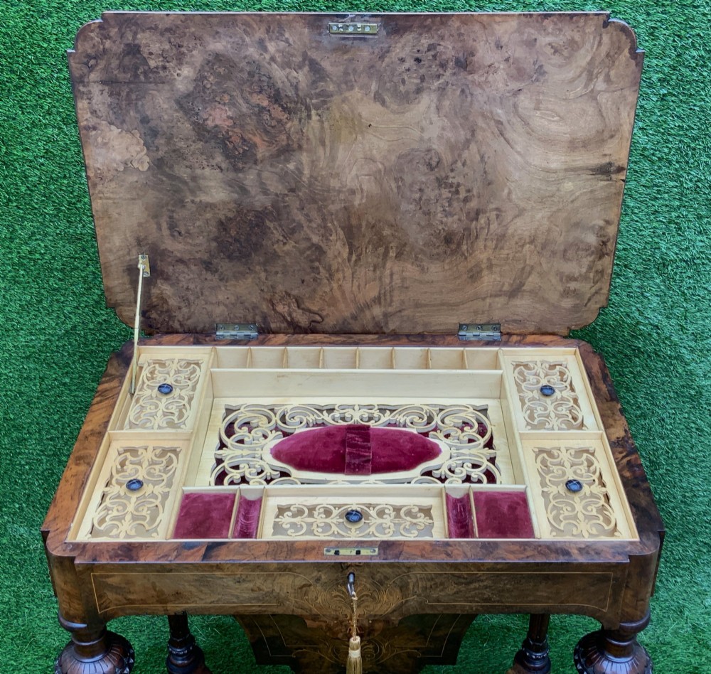 A 19th-century burr walnut work table featuring a green leather inset top, floral marquetry inlay, turned legs, and a hanging storage pouch. View V
