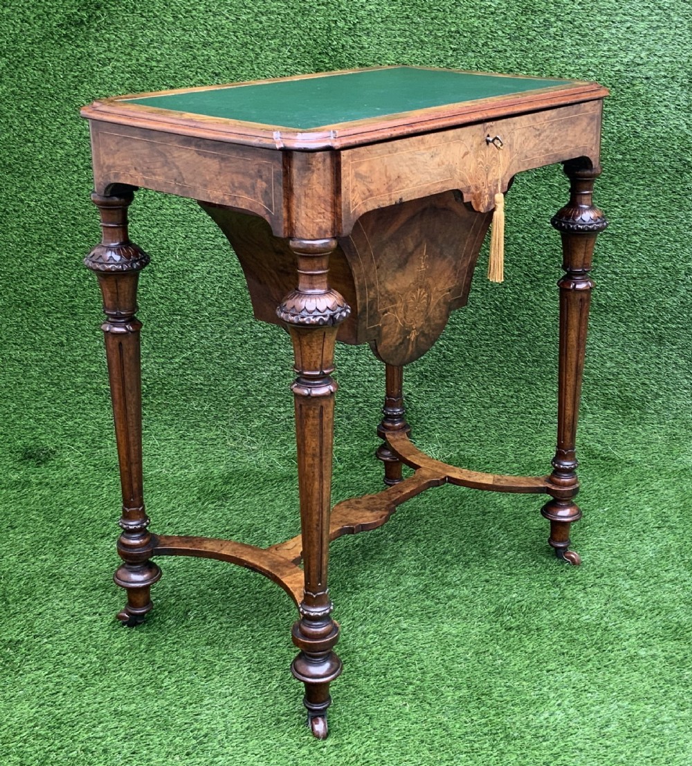 A 19th-century burr walnut work table featuring a green leather inset top, floral marquetry inlay, turned legs, and a hanging storage pouch. View X