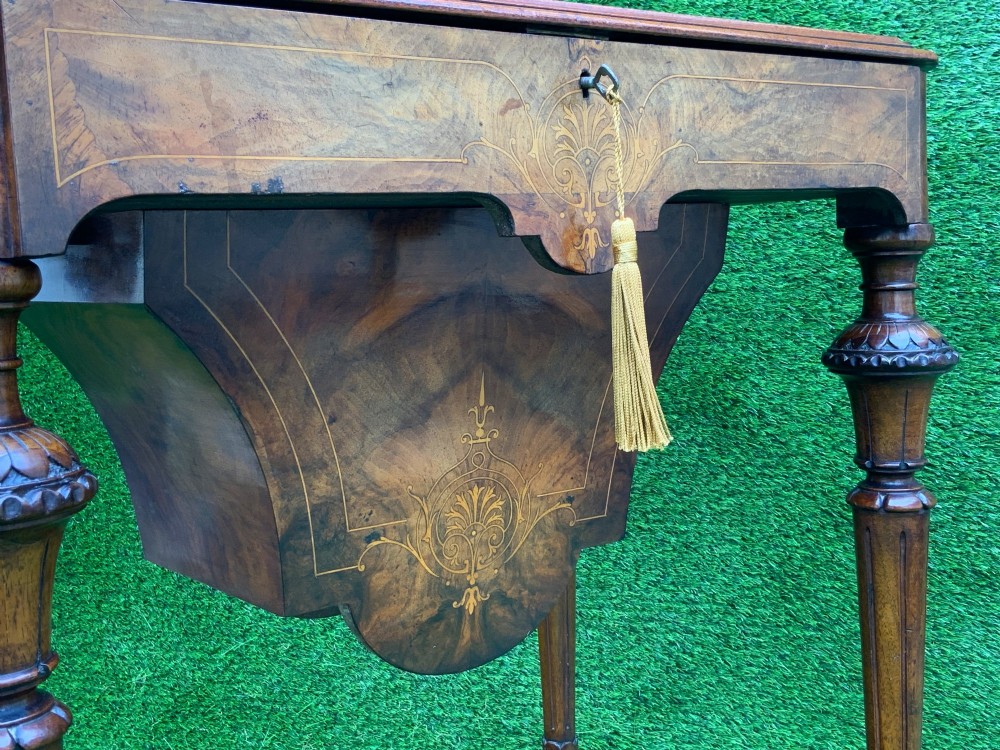 A 19th-century burr walnut work table featuring a green leather inset top, floral marquetry inlay, turned legs, and a hanging storage pouch. View XI